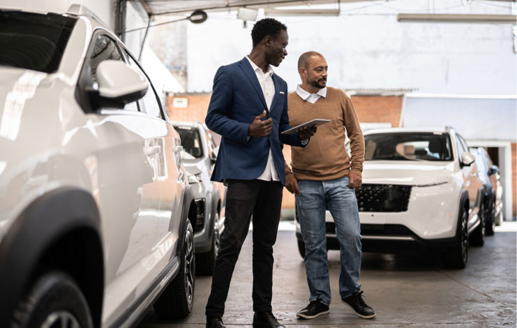 Salesman with a tablet in hand is showing a car to a customer in a car dealership