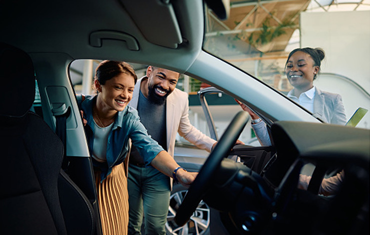 Young woman and man happily look into a new car at a car dealership while the saleswoman stands beside them.